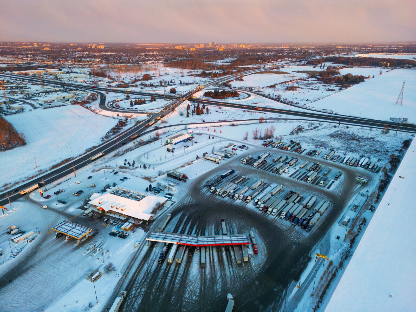 Aerial view of a snow-covered commercial truck stop and highway interchange in winter